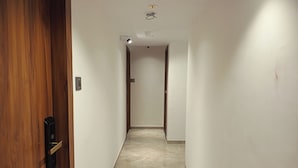A hallway with a wooden door on the left, a light fixture on the ceiling, and a tiled floor. - Hotel Preston (Mumbai)