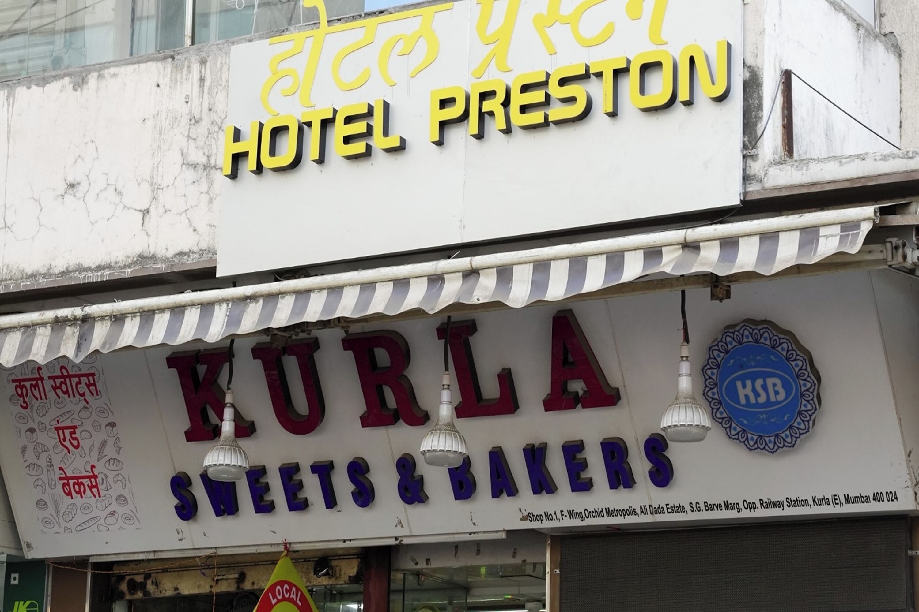 A sign for Hotel Preston and a shop named Kurla Sweets & Bakers.