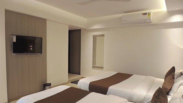 A hotel room with two beds, a TV, an air conditioning unit, and a mirror. - Hotel Preston (Mumbai)