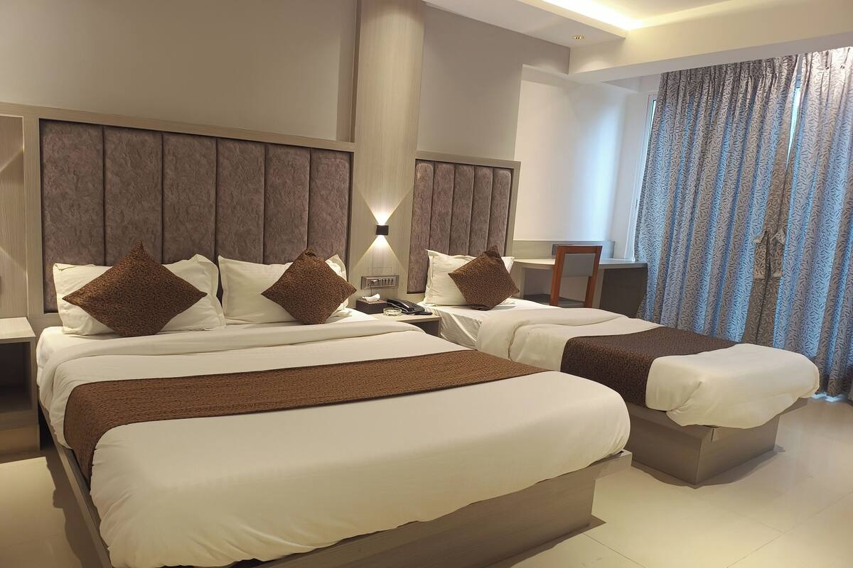 A hotel room with two beds, each with a brown headboard, white bedding, and a brown throw blanket. There is a nightstand with a lamp and a phone on one bed.