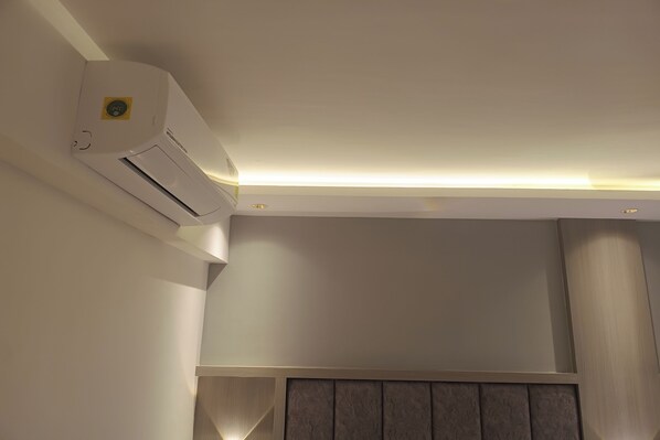 Une pièce avec un climatiseur blanc fixé au mur, un spot encastré au plafond et un mur de couleur neutre orné d’un motif en panneaux.