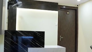 A hotel room with a marble vanity, a standing fan, a wooden door with the number 101, and a wall-mounted light fixture. - Hotel Preston (Mumbai)