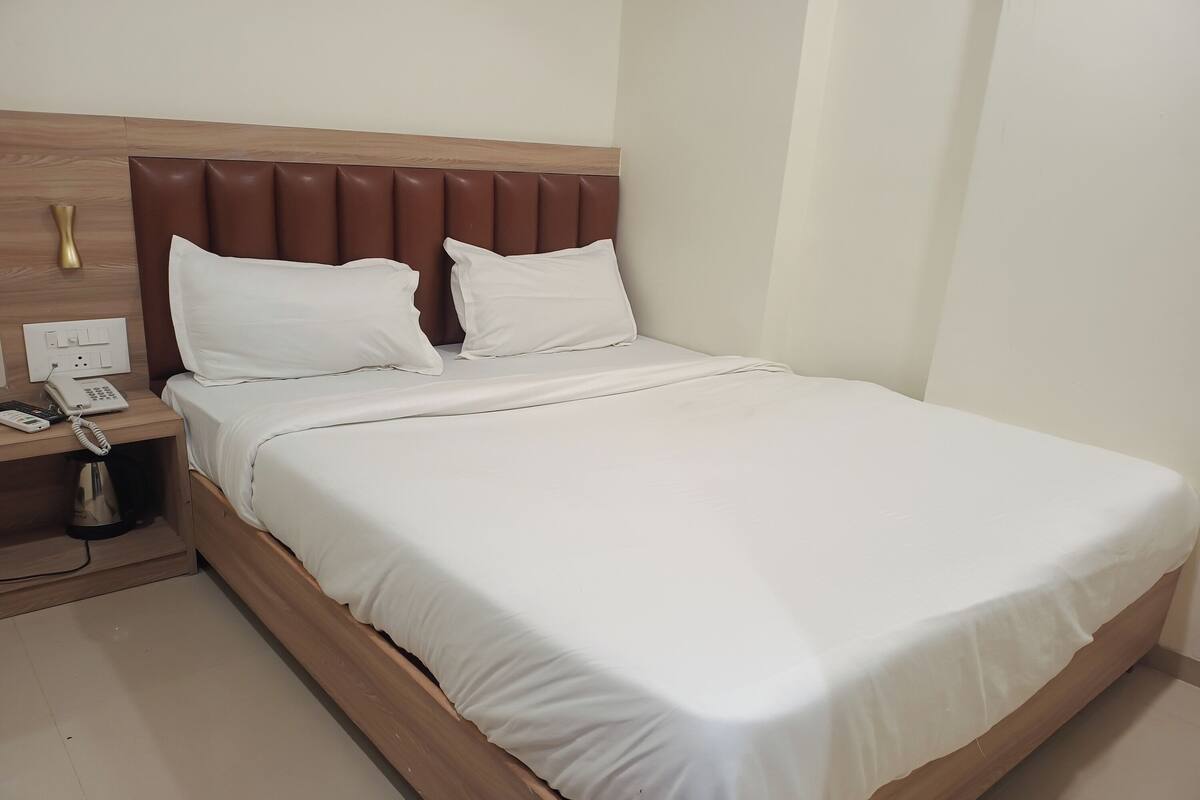 A neatly made bed with a wooden headboard, a bedside phone, and a small table with a kettle.