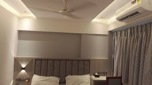 A hotel room with a bed, bedside table, lamp, and an air conditioning unit. - Hotel Preston (Mumbai)