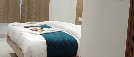 A modern bedroom with a wooden bed, white bedding, a teal throw, and a window with beige curtains.