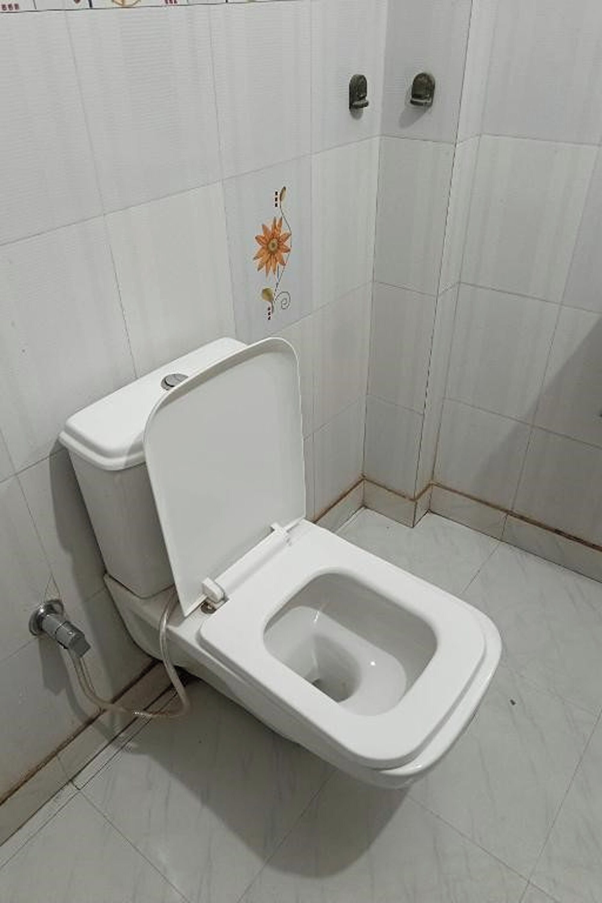 A white toilet with a closed lid in a bathroom with white tiles and a floral design on the wall.