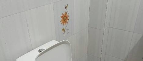 A white toilet with a closed lid in a bathroom with white tiles and a floral design on the wall.