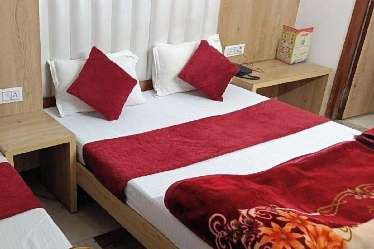 A hotel room with a wooden bed, white and red bedding, and a small bedside table with a book and a lamp.