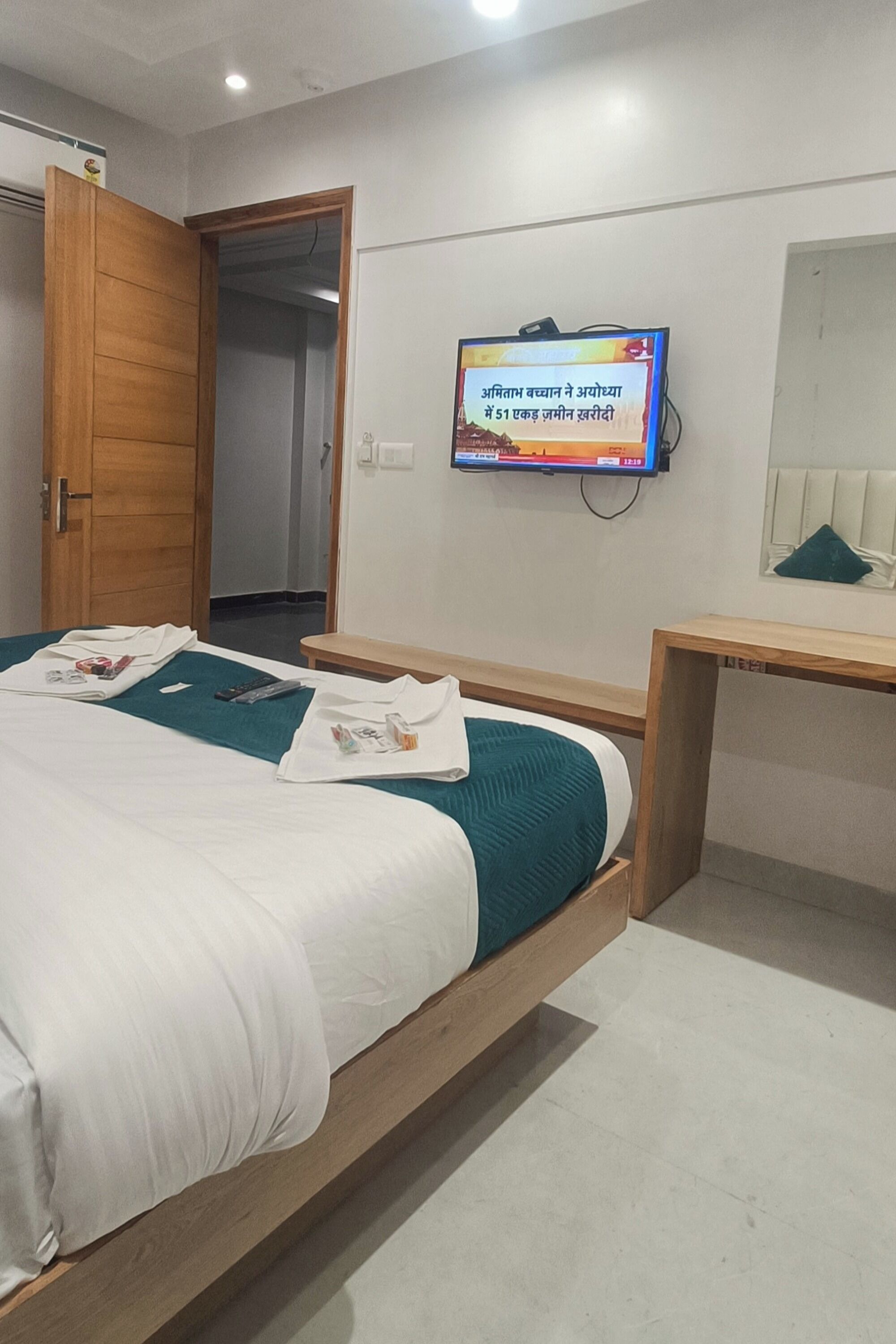 A hotel room with a wooden bed, a television mounted on the wall, and a wooden nightstand.
