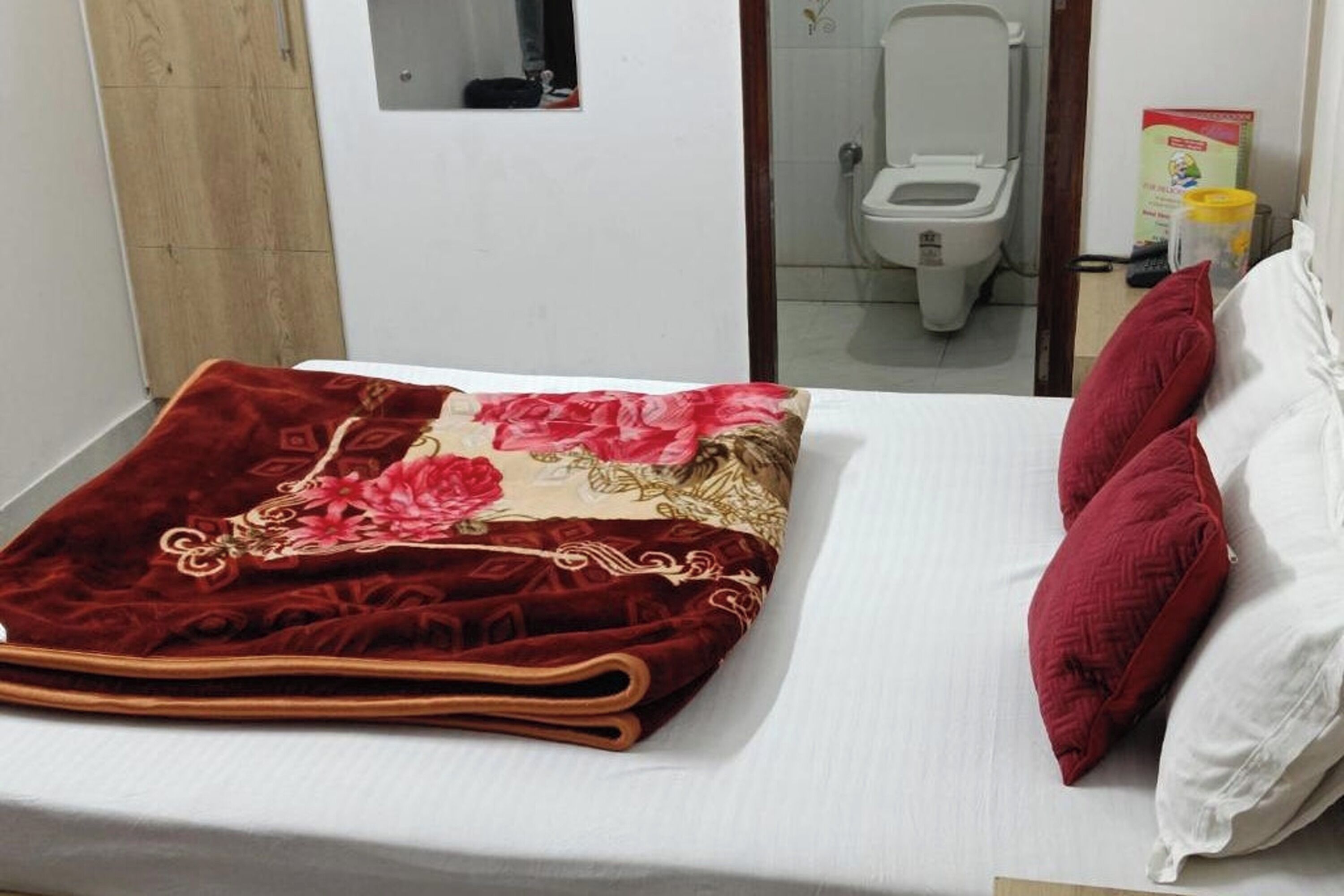 A neatly made bed with a red and beige blanket, two red pillows, and a white pillow.