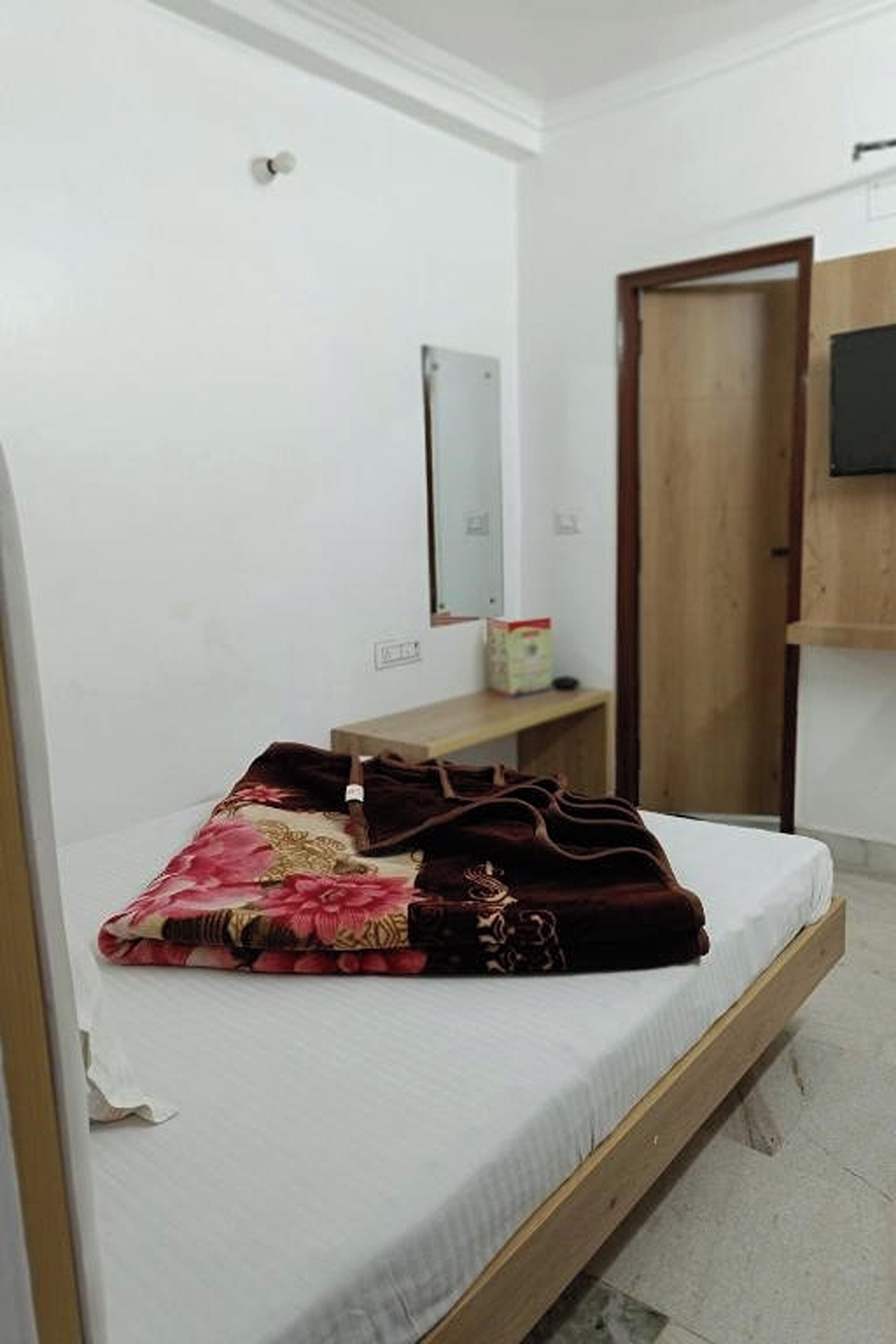 A bedroom with a single bed, a wooden headboard, a small bedside table, a mirror, and a wardrobe.