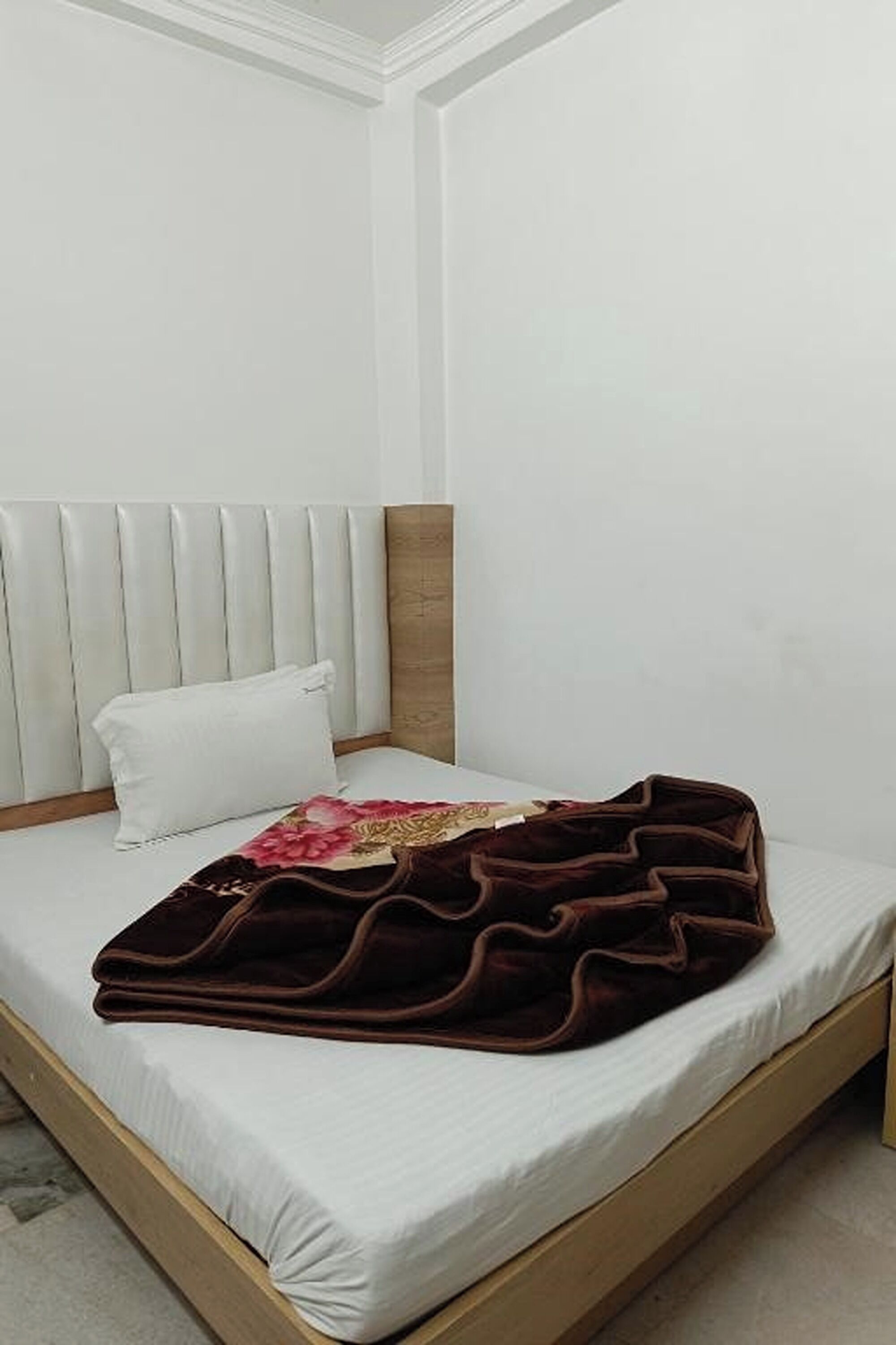 A single bed with a headboard, a white pillow, and a brown blanket.