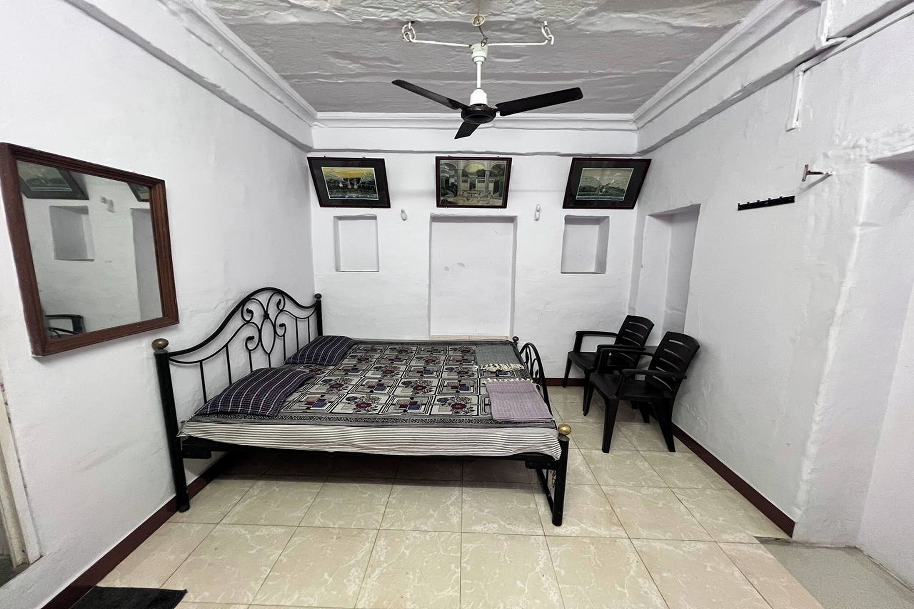 Una habitación con cama, ventilador de techo, espejo y tres cuadros en la pared.