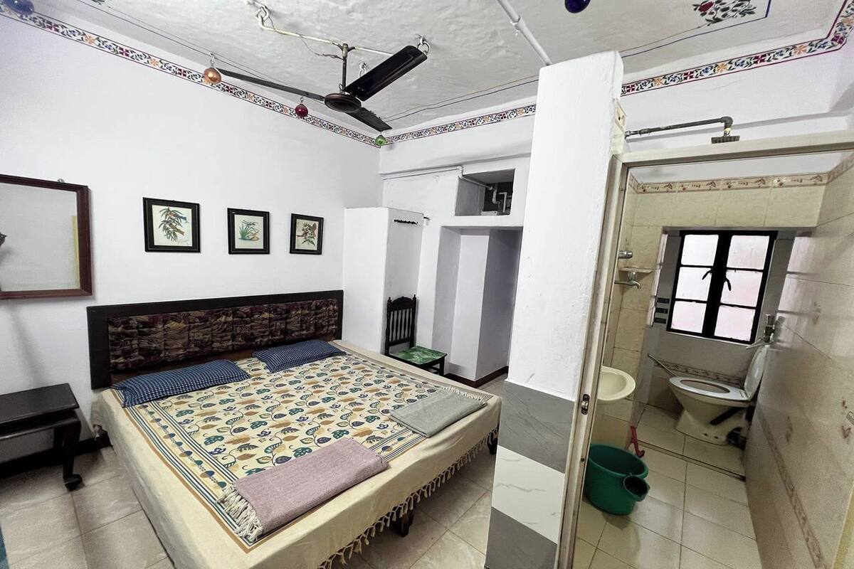 A bedroom with a bed, a desk, and a bathroom with a toilet and sink.