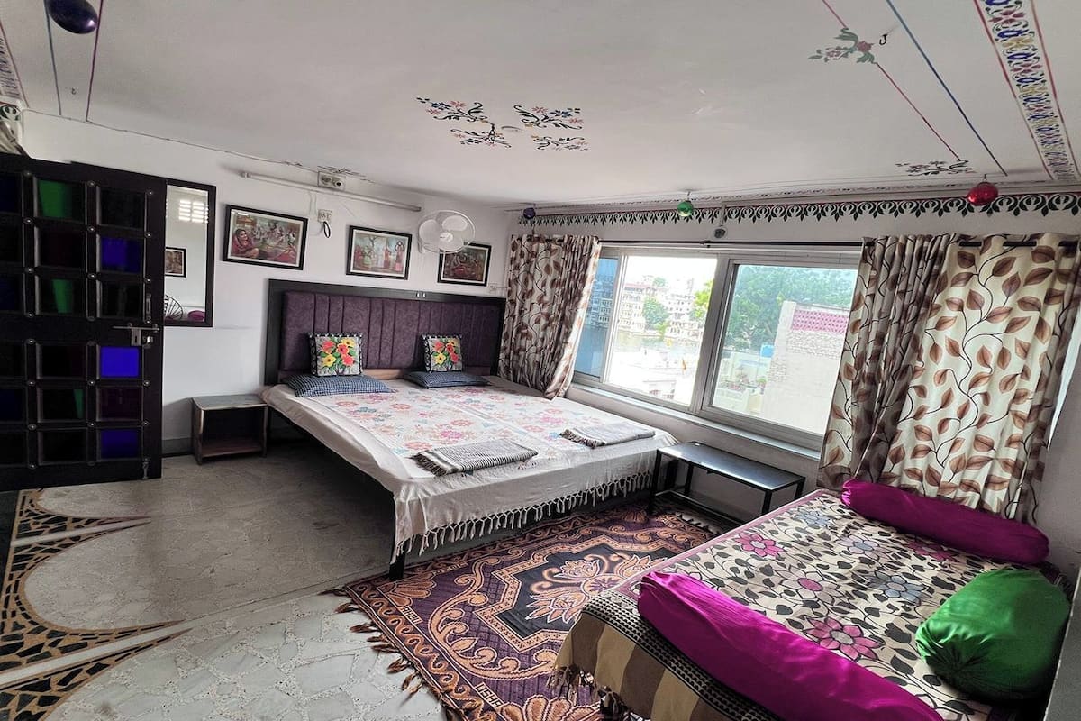 A bedroom with a bed, a desk, a window with curtains, and a patterned rug.