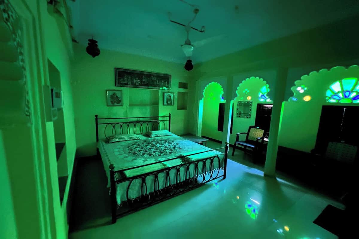 A room with a bed, a chair, and a table. There are decorative arches and a ceiling fan.