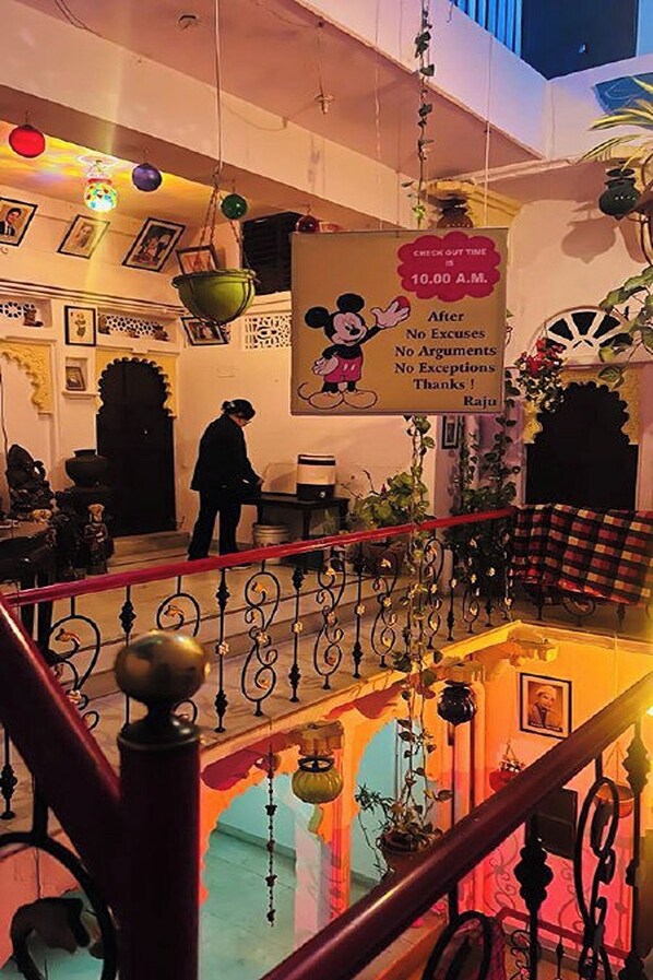 Un hall d’hôtel avec un panneau indiquant l’heure limite pour quitter les lieux, un escalier orné de rampes décoratives et divers objets de décoration.