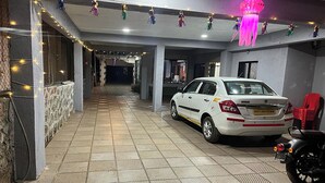 A covered parking area with a white car and a motorcycle, decorated with string lights and hanging ornaments. - Savitri Bungalow (Jaoli)