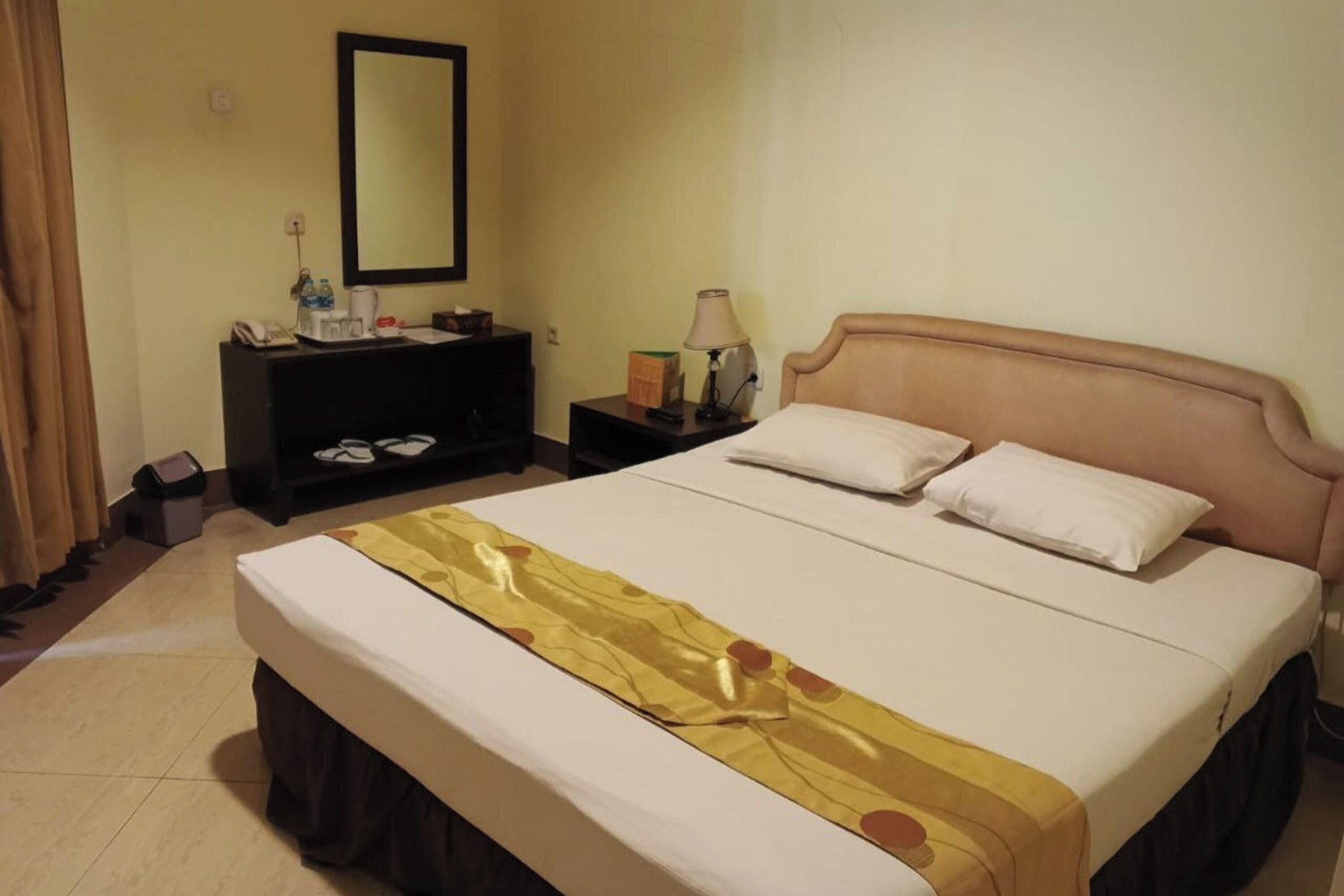 A hotel room with a bed, a bedside table, a lamp, a mirror, and a dresser.