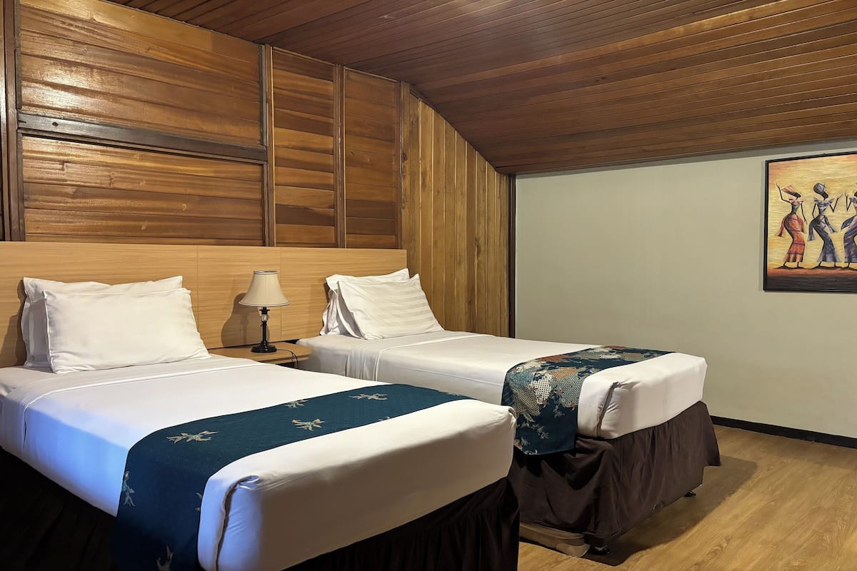 A hotel room with two single beds, wooden paneling on the walls, a painting on the wall, and a wooden floor.