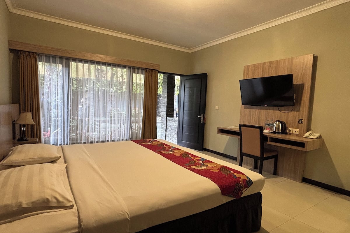 A hotel room with a large bed, a desk with a chair, a television mounted on the wall, and a window with curtains.