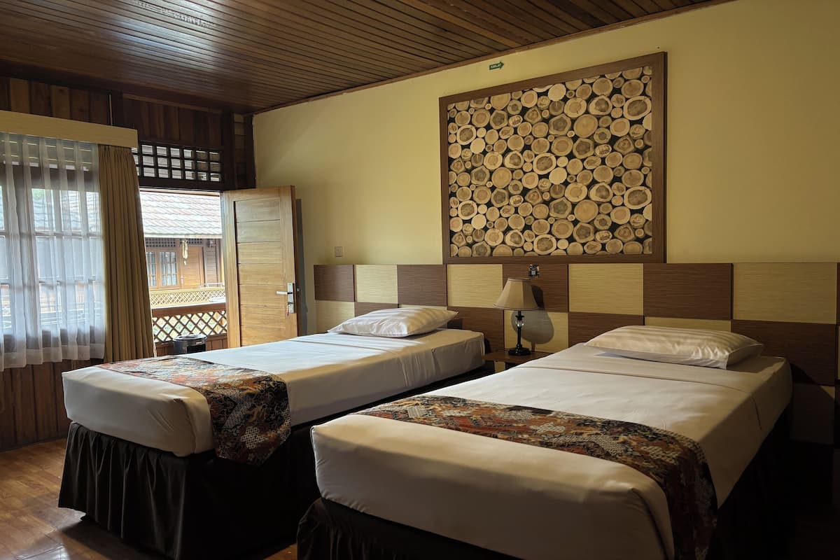 A hotel room with two single beds, a wooden headboard, a wall-mounted log art piece, and a window with curtains.