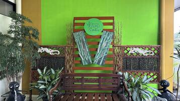 Un banco de madera con un fondo verde, un letrero que dice "Hotel Pesoma Barine" y paneles decorativos con motivos vegetales.