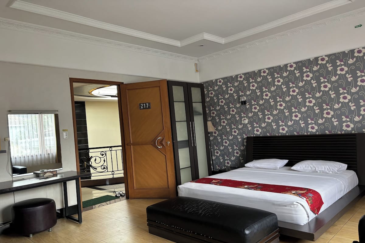 A hotel room with a bed, a desk, a mirror, a wardrobe, and a door to another room.