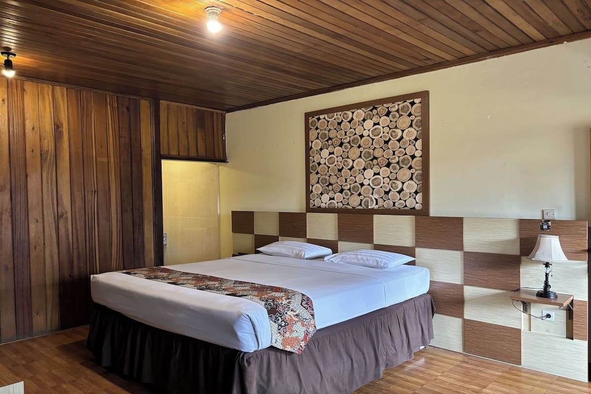 A bedroom with a wooden ceiling, a bed with a patterned bedspread, a wall-mounted log art piece, and a bedside lamp.