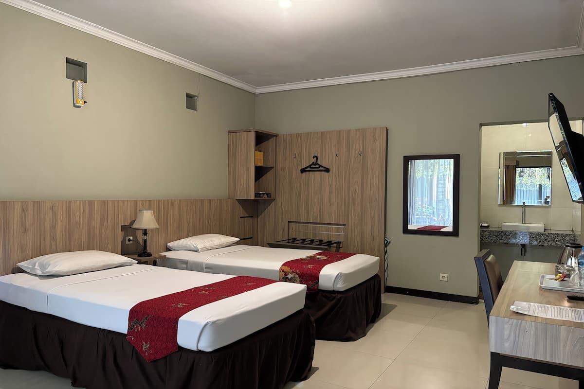 A hotel room with two beds, a desk, a mirror, and a window.