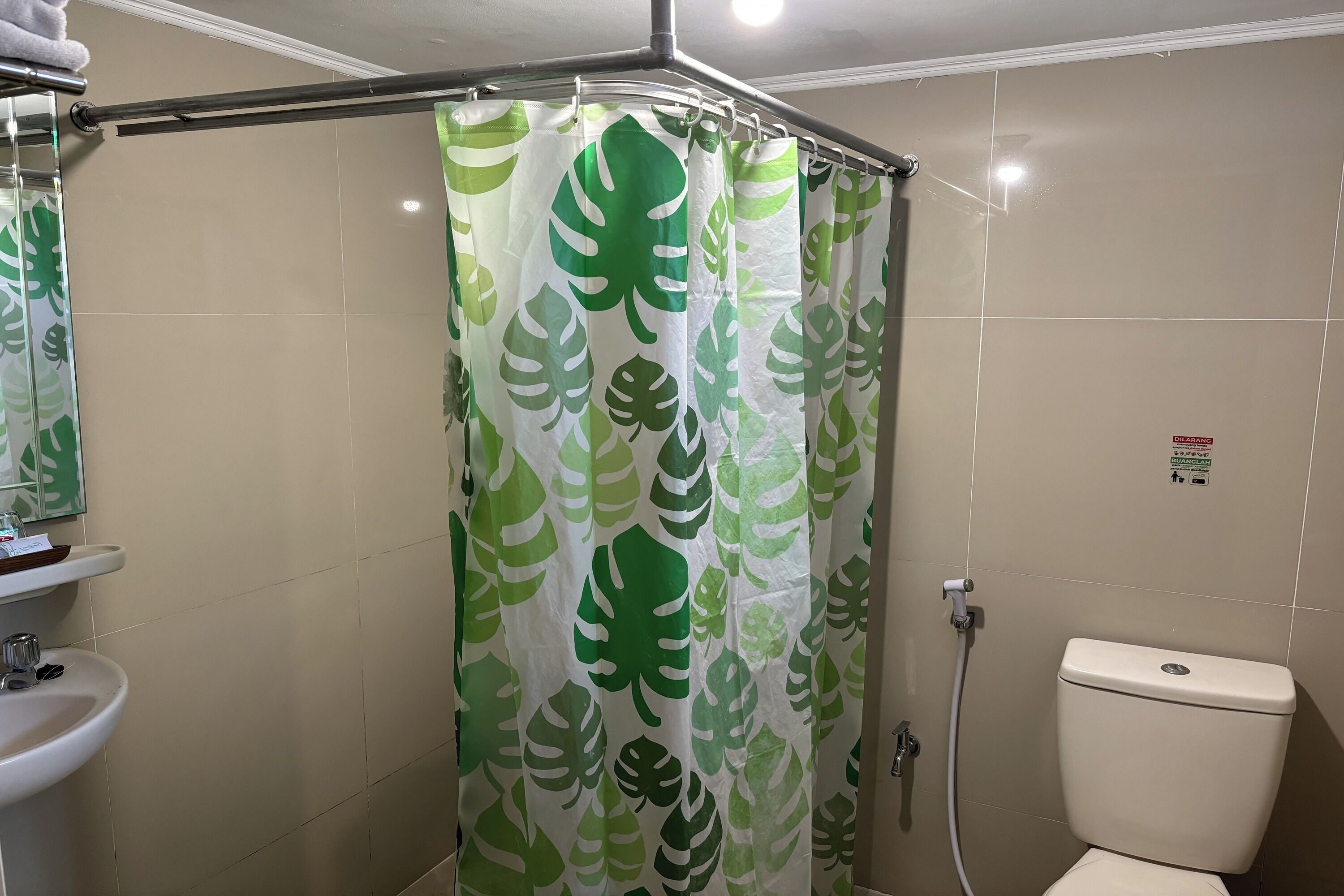 Un baño con cortina de ducha estampada con hojas, un inodoro y un lavabo con espejo superior.