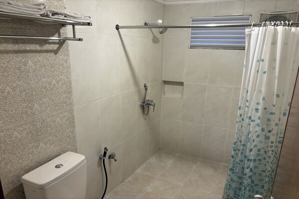 Une petite cabine de douche carrelée, équipée de toilettes, d’un porte-serviettes et d’un rideau de douche.