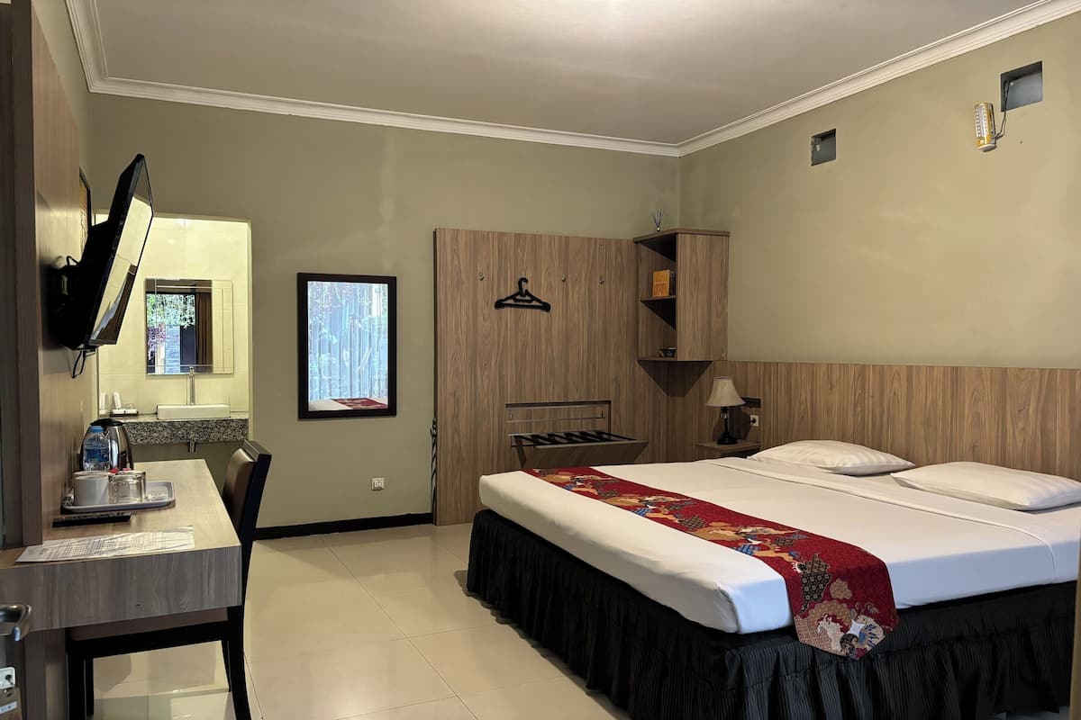 A hotel room with a bed, a desk with a computer, a TV, and a wardrobe.