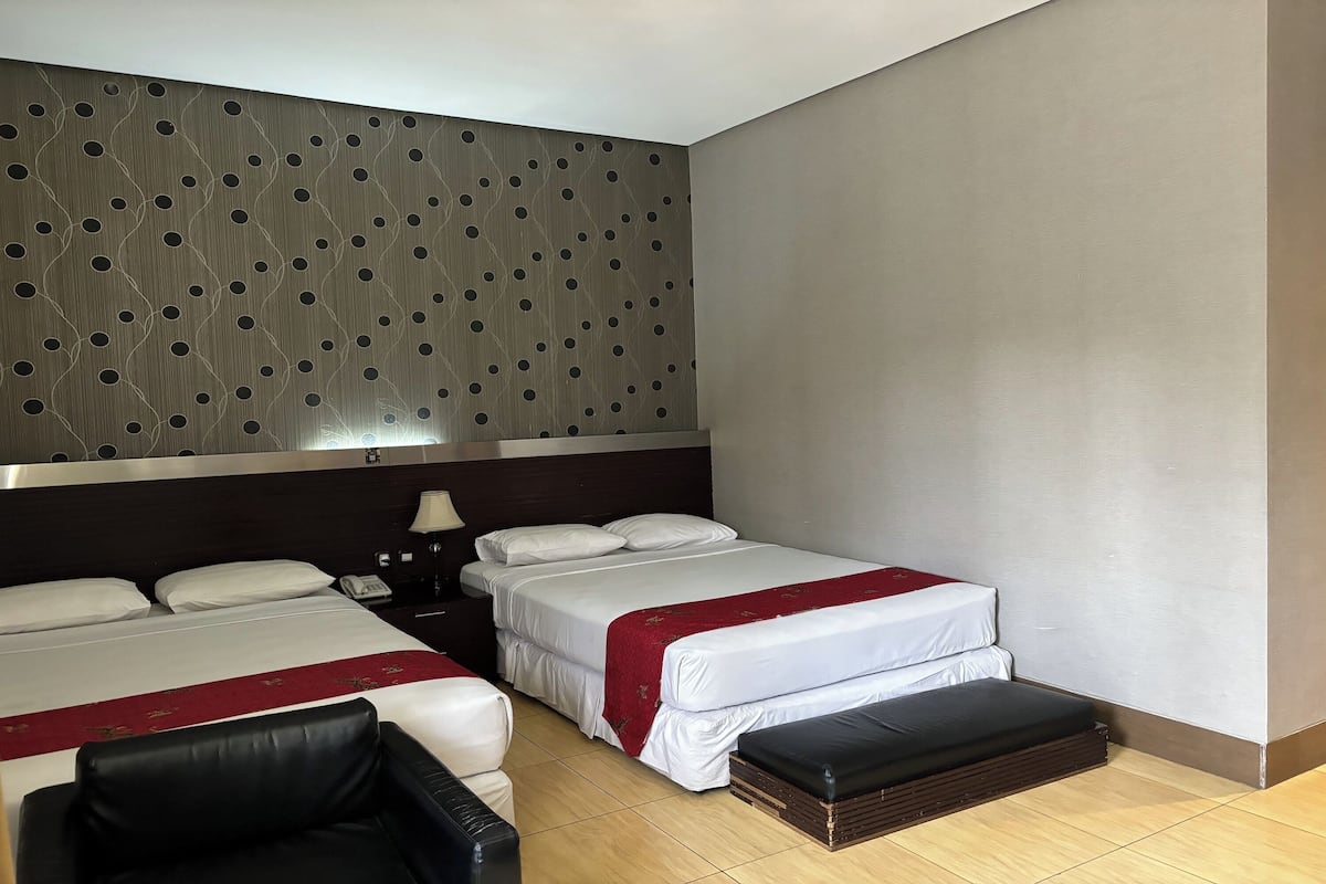 A hotel room with two beds, a desk, a chair, a nightstand, and a wall with a geometric pattern.
