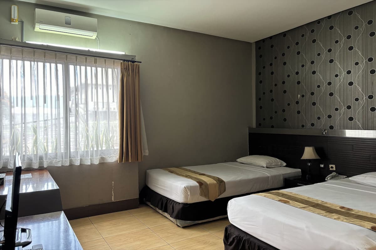 A hotel room with two beds, a desk, a chair, a TV, and an air conditioning unit.