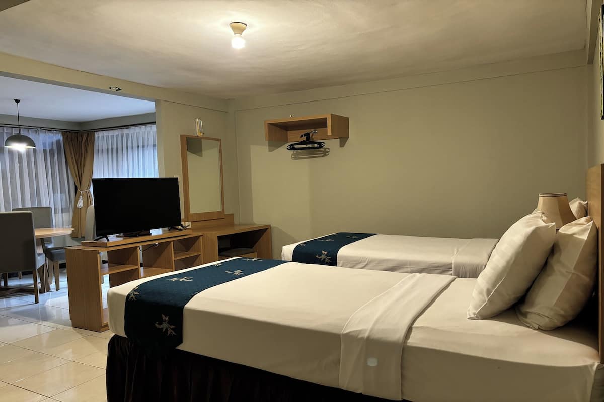 A hotel room with two beds, a desk with a television, a mirror, and a small shelf.