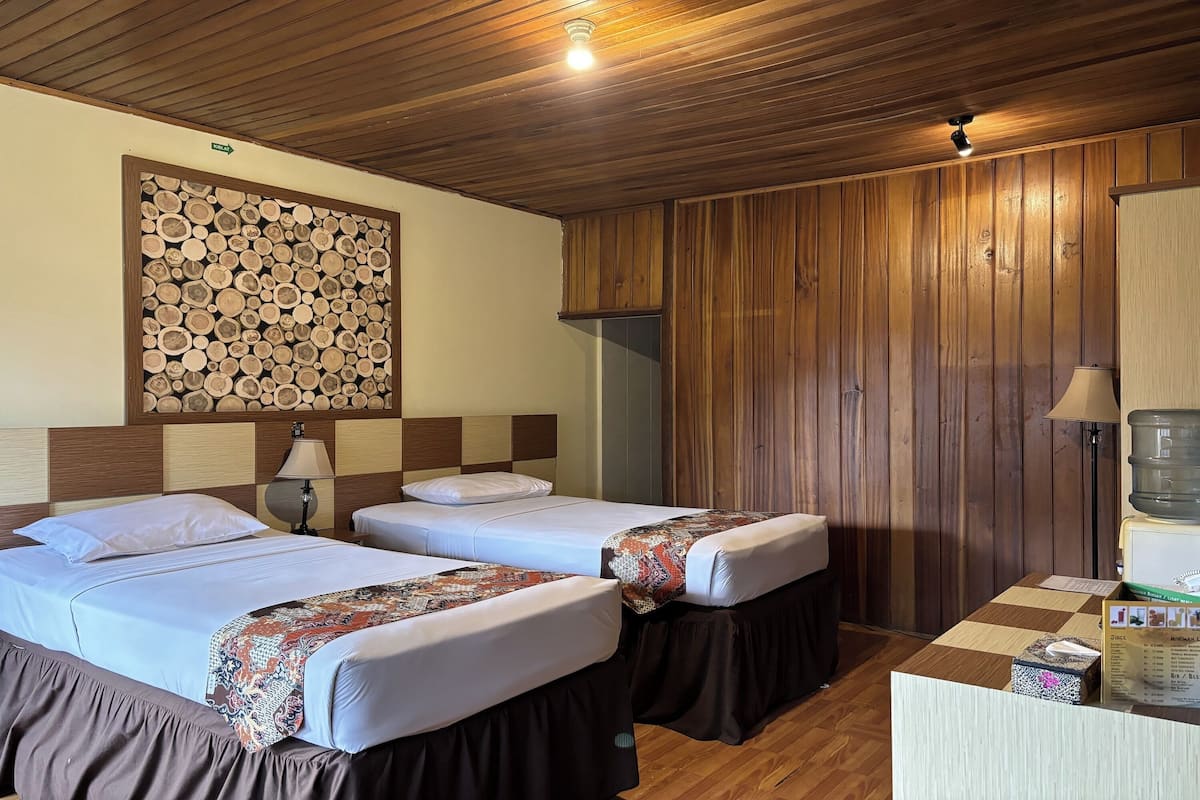 A room with two beds, wooden paneling, a wall-mounted log display, a desk with a lamp, and a water dispenser.