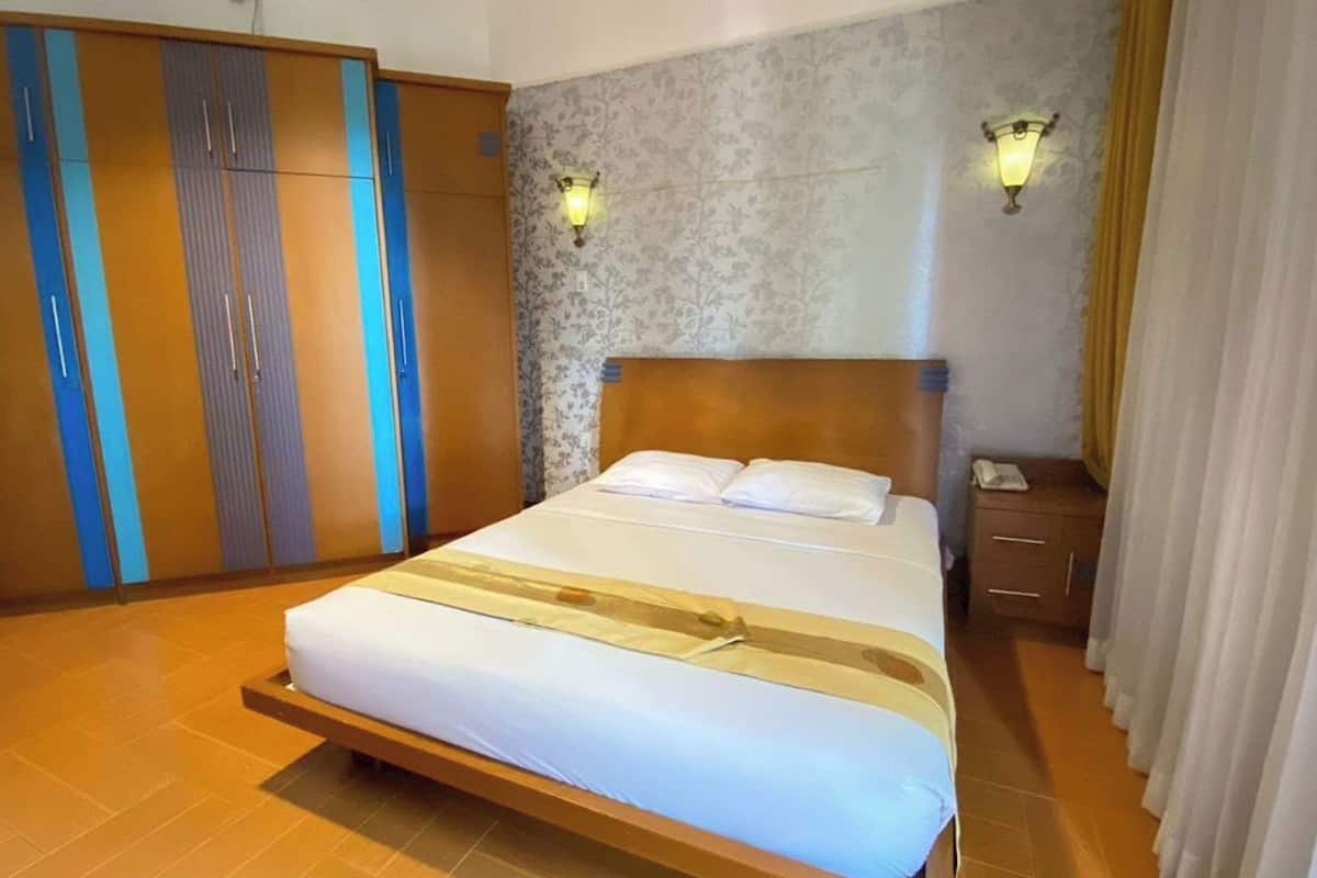 A hotel room with a bed, a wardrobe, a nightstand, and two wall-mounted lamps.