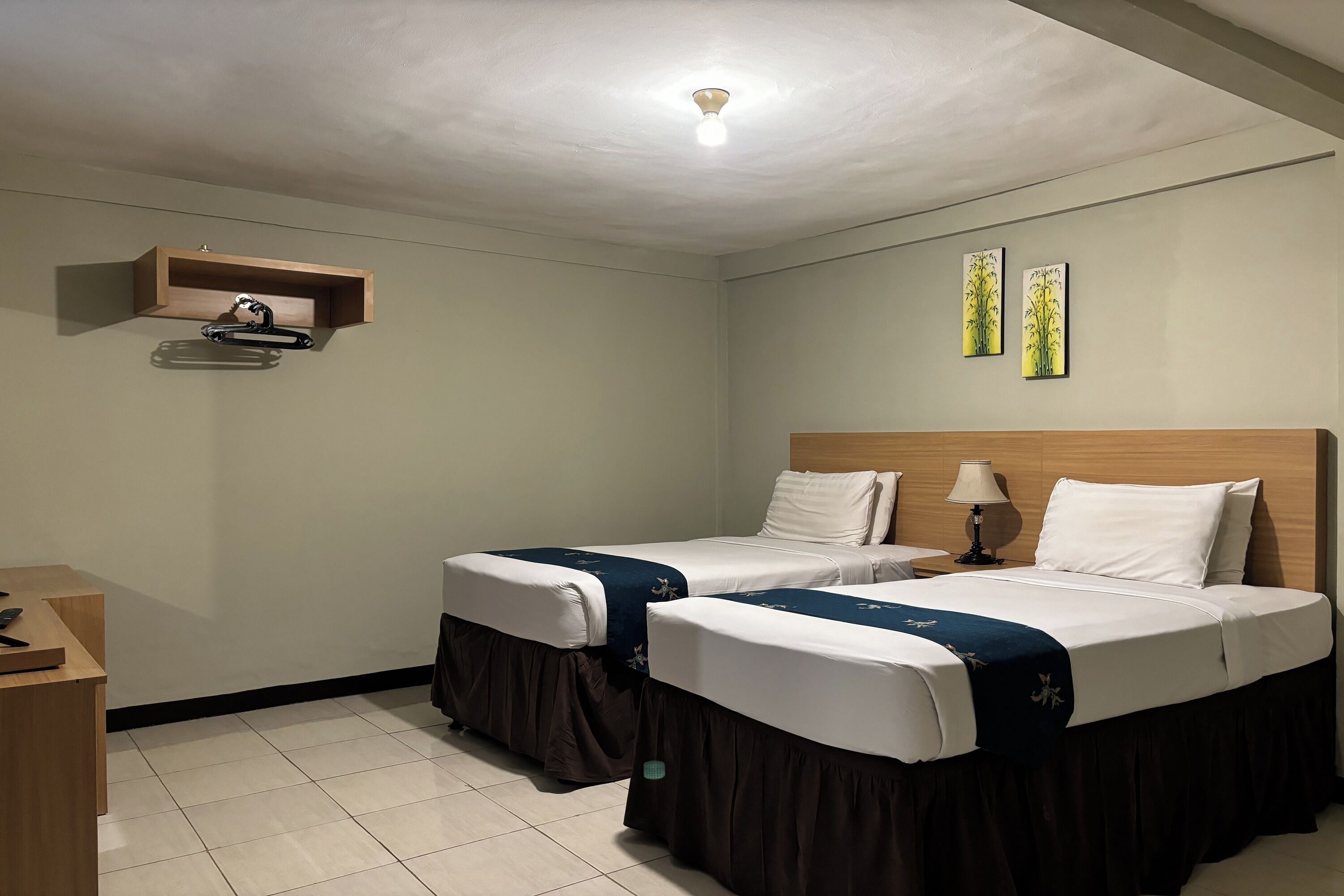 Une chambre d’hôtel avec deux lits, une tête de lit en bois, une table de chevet avec une lampe et une petite étagère avec une autre lampe.