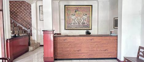Un espace d’accueil avec un comptoir de réception en bois, un escalier orné de papier peint à motifs et une œuvre d’art encadrée accrochée au mur.