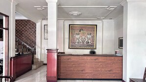 Un espace d’accueil avec un comptoir de réception en bois, un escalier agrémenté d’un mur décoratif et une œuvre d’art encadrée accrochée au mur.