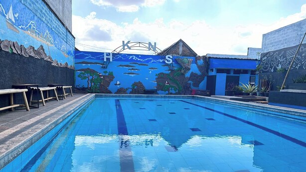 Une piscine avec une fresque murale sur le mur adjacent, des bancs et des plantes en pot.