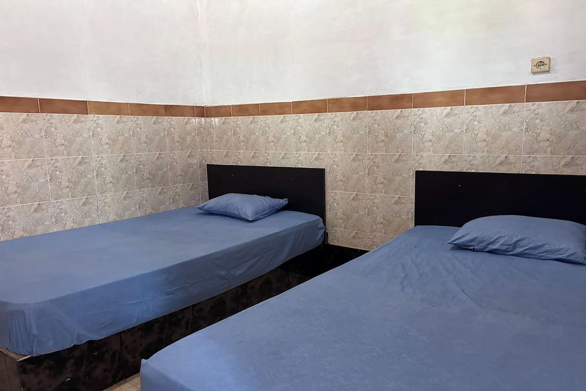 Two single beds with headboards, a tiled wall, and a small electrical outlet on the ceiling.