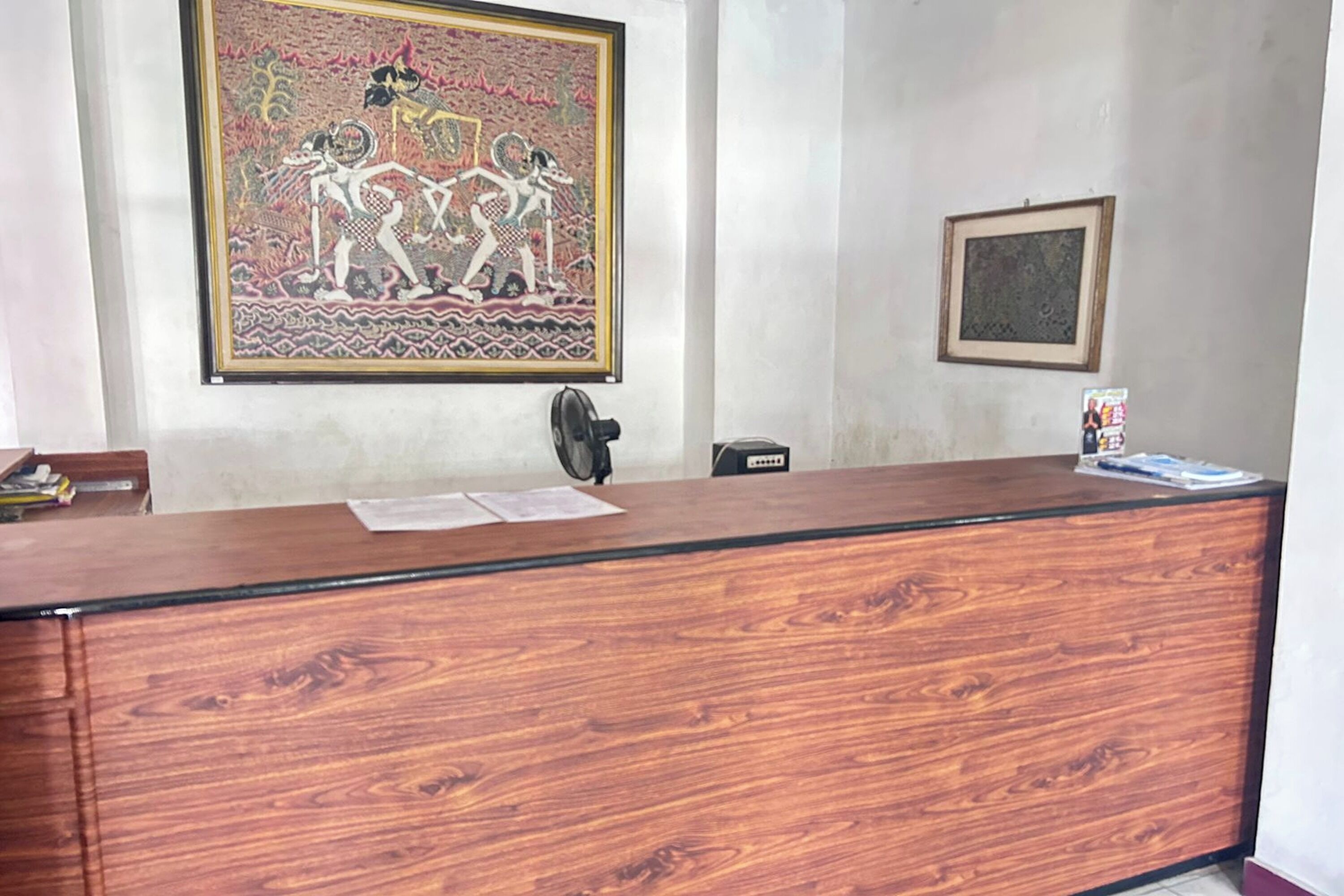 Un comptoir d’accueil surmonté d’une œuvre d’art encadrée, un petit tableau encadré accroché au mur et quelques objets posés sur le comptoir.