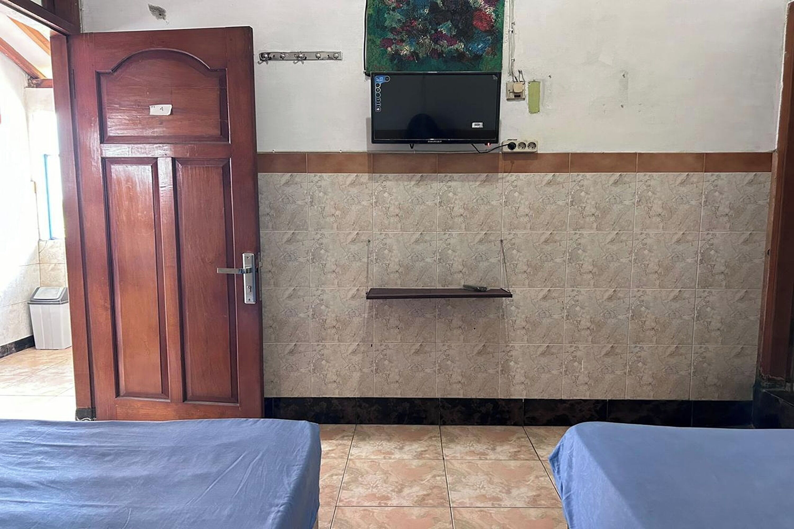 A room with two beds, a wooden door, a television mounted on the wall, and a tiled floor.