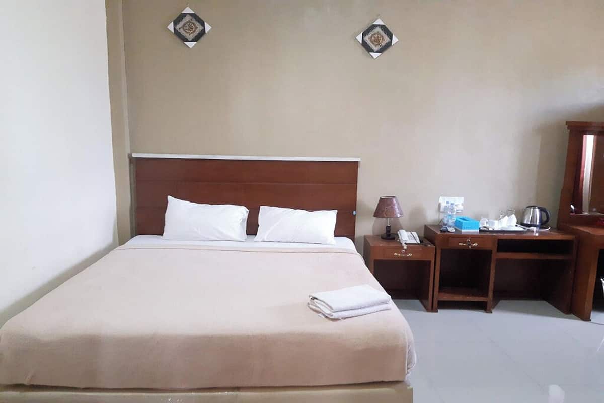 Habitación de hotel con una cama grande, una mesita de noche con lámpara, un escritorio con silla y un espejo.