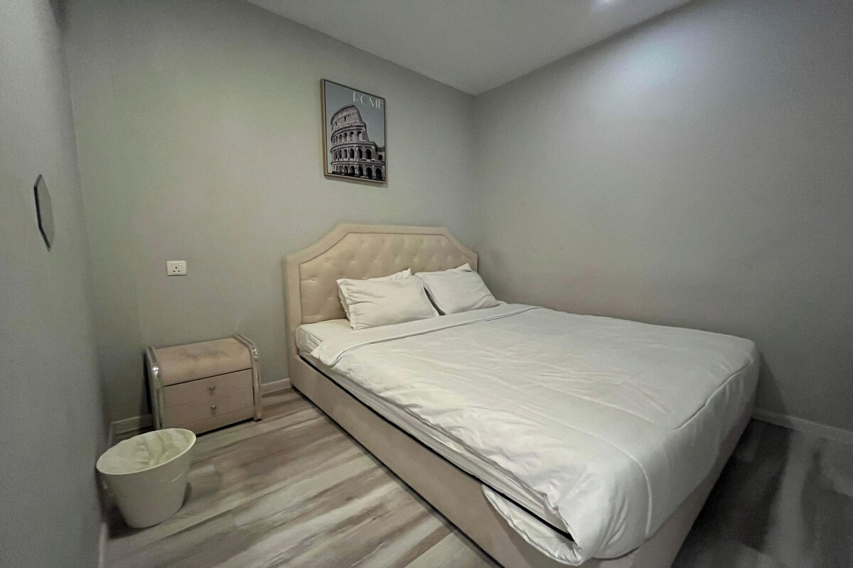 Une chambre à coucher comprenant un lit, une table de chevet, une poubelle et un tableau accroché au mur.
