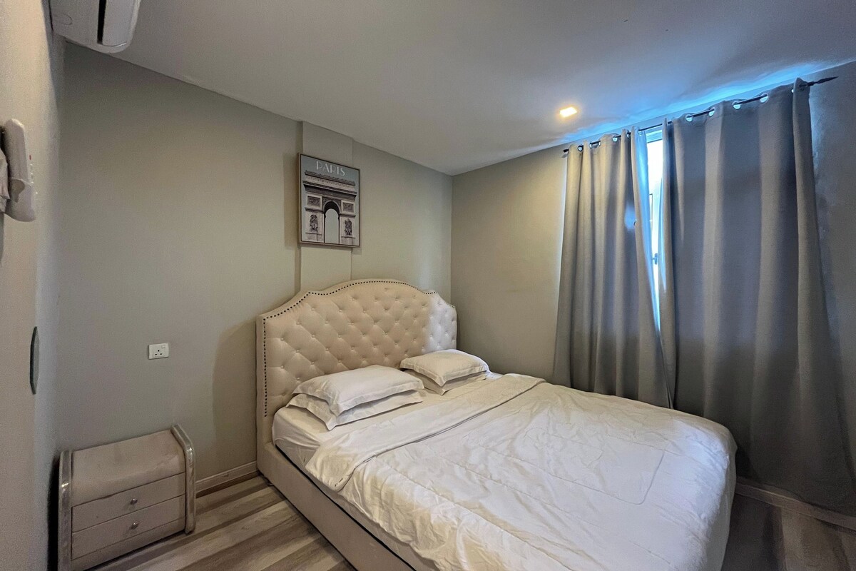 A bedroom with a tufted headboard, a bed with white bedding, a small bedside table with drawers, and a wall-mounted air conditioning unit.