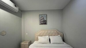 A bedroom with a bed, a nightstand, a trash bin, and a wall-mounted air conditioner. - Casanova (Batam)