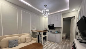A compact living space with a sofa, a wooden table, a kitchenette, and a TV. - Casanova (Batam)